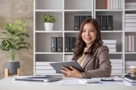 Cheerful business lady working on laptop in office, Asian happy beautiful businesswoman in formal suit work in workplace. Attractive female employee office worker smile...