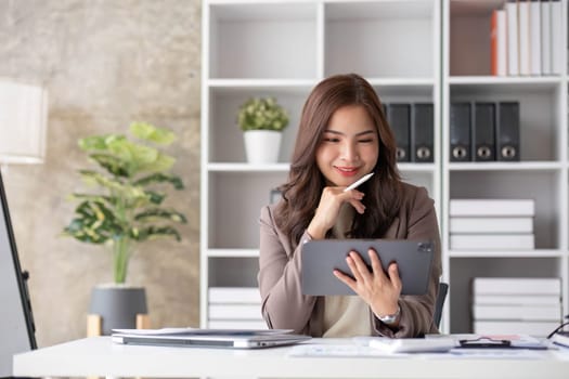 Cheerful business lady working on laptop in office, Asian happy beautiful businesswoman in formal suit work in workplace. Attractive female employee office worker smile...