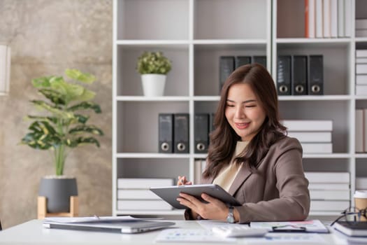 Cheerful business lady working on laptop in office, Asian happy beautiful businesswoman in formal suit work in workplace. Attractive female employee office worker smile...