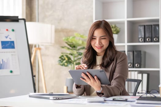 Cheerful business lady working on laptop in office, Asian happy beautiful businesswoman in formal suit work in workplace. Attractive female employee office worker smile...