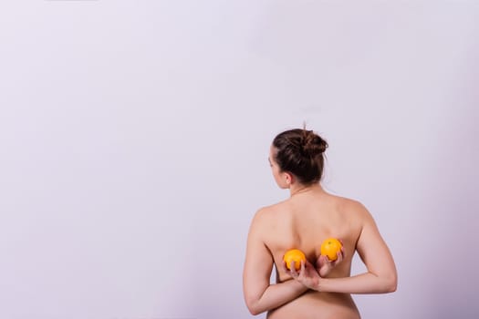 Slim woman is holding orange. Perfect female back without any cellulite.