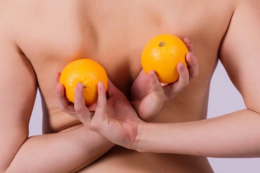 Slim woman is holding orange. Perfect female back without any cellulite.