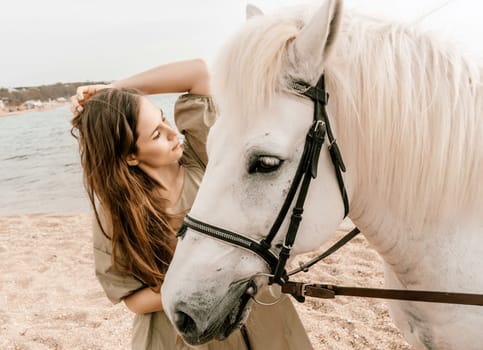 A woman in a dress stands next to a white horse on a beach, with the blue sky and sea in the background