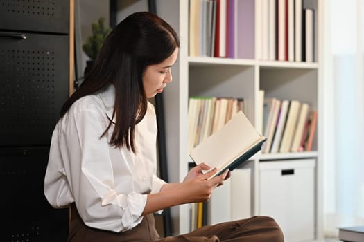 Image of calm young asian woman wearing casual clothes reading book, spending free spare time at home.