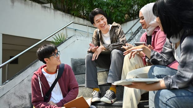 Group of college students sitting on stairs chatting and laughing during break . Education and youth lifestyle concept.