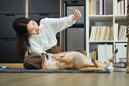 Beautiful woman using smartphone taking selfie with cute dog lying floor at home. Technology, people and animals concept.