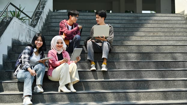 Group of students talking to each other after classes while sitting in front of university building.