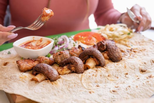 Woman eating grilled kebab with pita bread and vegetables on tray in summer fast food street cafe. shawarma in pit of fresh vegetables and meat. National Armenian food