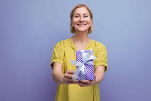 smiling blonde 50s woman holding out a gift box with a bow for a surprise.