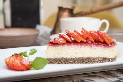 Piece of delicious cheesecake with berries on real cafe table close up. Cup of coffee on the background