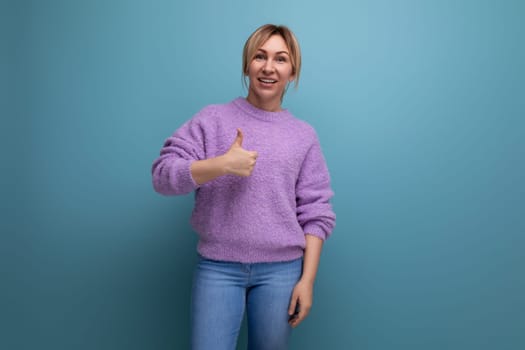nice cute blond young woman consultant in purple sweater showing super class thumbs up on blue background with copy space.