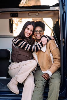 portrait of two happy women in a camper van embracing and smiling looking at camera, concept of weekend getaway and female friendship