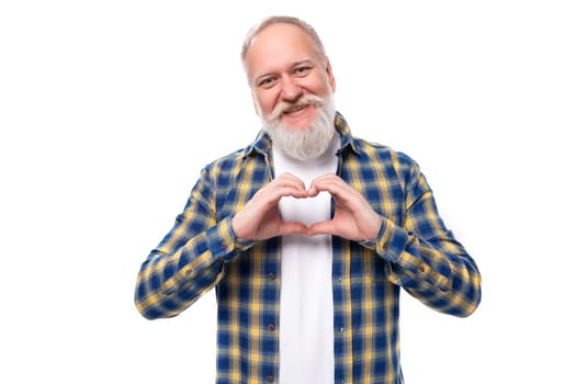 cute mature gray-haired man with a beard in a shirt shows a heart with his hands on a white background.