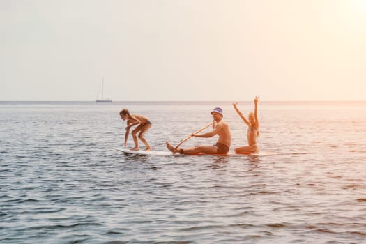 Father and his adorable little son and daughter sitting on stand up board having fun during summer beach vacation