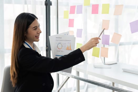 Happy business female planning ideas on a glass wall with colorful sticky notes inside a office.