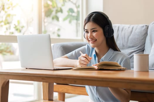 young woman working on laptop and taking notes while listening to lecture at home.