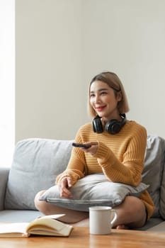 Asian young beautiful woman watching fun movie on television at home. Attractive casual girl feel happy and relax sit on sofa.