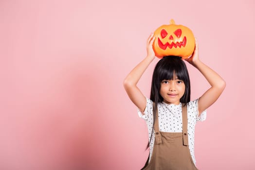 Asian little kid 10 years old holding carved Halloween pumpkin at studio shot isolated on pink background, Portrait of happy child girl smiling show Jack O pumpkin, Concept for Halloween holiday