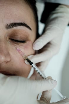 Cosmetologist applying eye mesotherapy to female patient. Eye mesotherapy procedure. Serum being applied in the undereye area via a syringe.