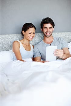 Taking technology to bed. Attractive couple in bed looking at a digital tablet