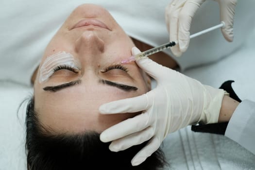 Top view of female patient having eye mesotheraphy applied. Eye mesotherapy procedure. Serum being applied in the undereye area via a syringe.