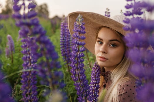 A beautiful woman in a straw hat walks in a field with purple flowers. A walk in nature in the lupin field.