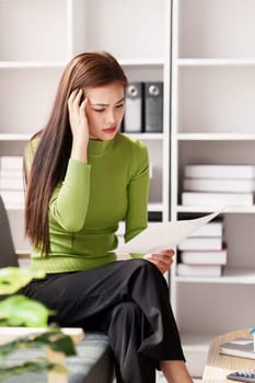 Stressed woman sits on sofa at home, studying and analyze house bills and submitting tax forms..