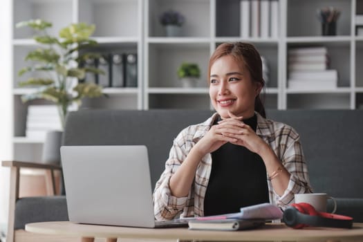 Beautiful and inspired Asian woman working on her tasks on laptop in a living room on the weekend...