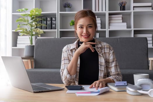 Beautiful and inspired Asian woman working on her tasks on laptop in a living room on the weekend...