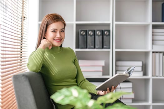 Attractive young Asian woman sits in the minimal and comfortable living room enjoying reading a book...