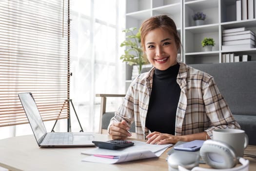 Beautiful and inspired Asian woman working on her tasks on laptop in a living room on the weekend...