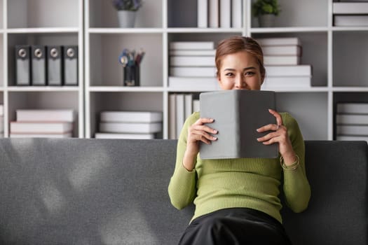 Attractive young Asian woman sits in the minimal and comfortable living room enjoying reading a book...