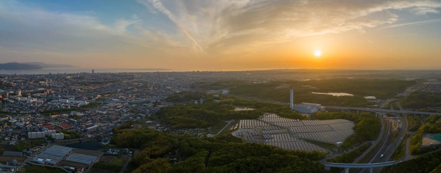 Sun sets on solar panels at small energy plant at edge of sprawling city. High quality photo