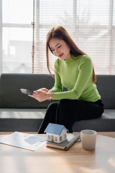 woman sitting on cozy sofa and planning and calculate expense and mortgage with calculator and home on desk, insurance and budget of residential, loan and residence, business and property concept