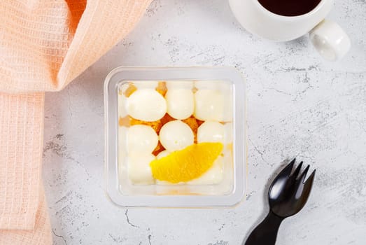 Dessert of cream, jam and orange in a plastic glass on a concrete background. High quality photo