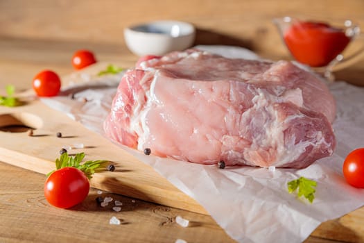 A piece of raw pork meat on a cutting board. Tomatoes, ketchup