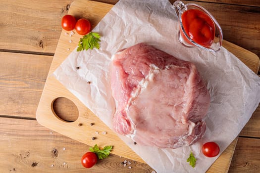 A piece of raw pork meat on a cutting board. Tomatoes, ketchup. View from above
