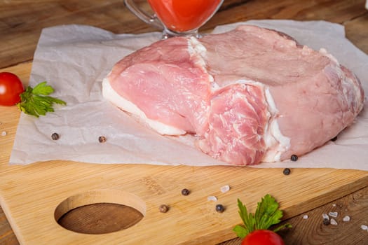 A piece of raw pork meat on a cutting board. Tomatoes, ketchup