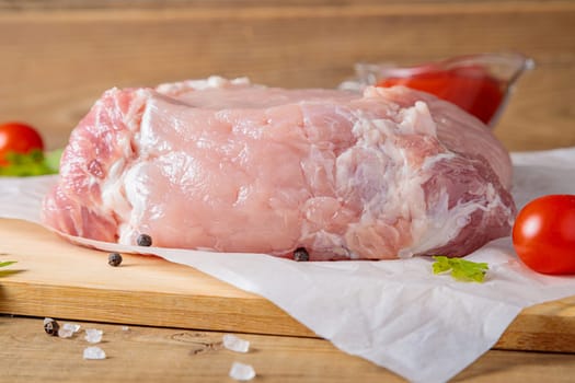 A piece of raw pork meat on a cutting board. Tomatoes, ketchup