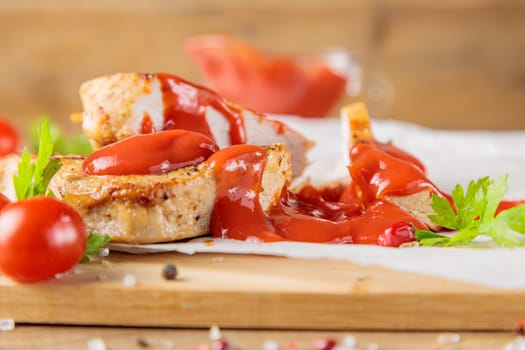 Slices of roast pork meat with tomato and ketchup on a wooden board