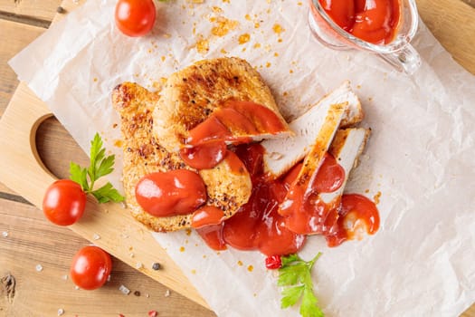 Slices of roast pork meat with tomato and ketchup on a wooden board. Top view