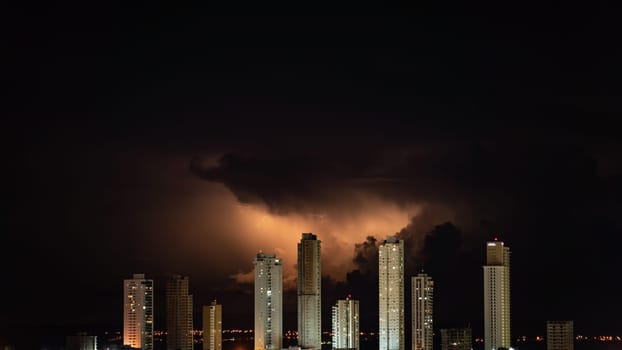 A red electric storm illuminates the dark night sky over a cityscape dominated by tall skyscrapers, creating a dramatic contrast. Space for text.
