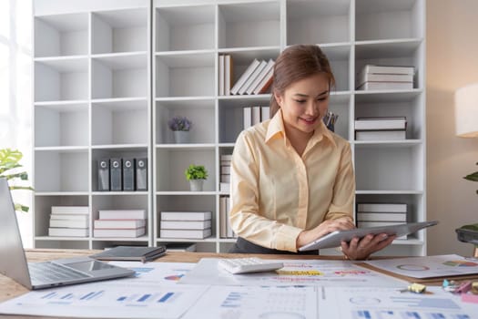 Beautiful and happy young Asian businesswoman looking at her laptop screen while enjoying her morning coffee at her desk in the office...