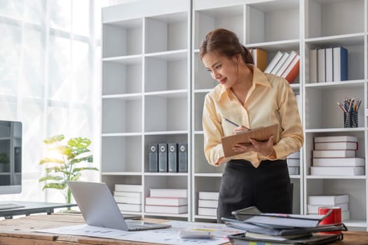 Excited business asian woman sitting at table with laptop and celebrating success..