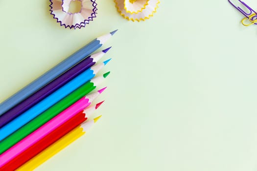 Colored pencils in the corner are sharpened with shavings and colored paper clips for office work and school on a light yellow background.