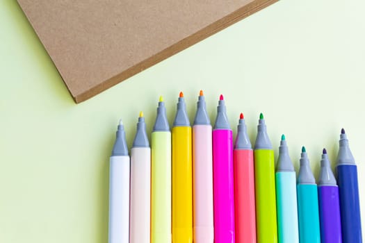 Multi-colored markers for sketching, for drawing drawings and objects, for working in the office and studying at school, with open caps and a sheet of craft paper on a light yellow background.