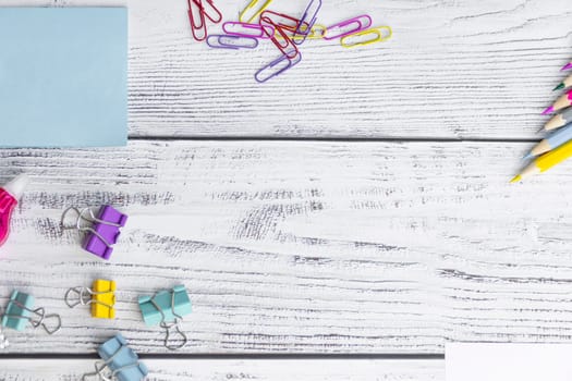 Blue sheets for notes, colored paper clips, colored pencils, paper clips and a proofreader for working in the office and studying at school on a light, wooden background.
