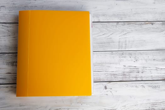 A bright, yellow, thick, stationery folder with a large number of documents for office work and university studies on a light, wooden background.