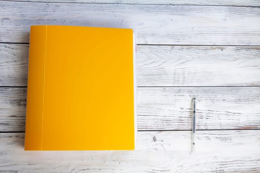 A bright, yellow, thick, stationery folder with a large number of documents and a ballpoint pen for office work and university studies on a light, wooden background.