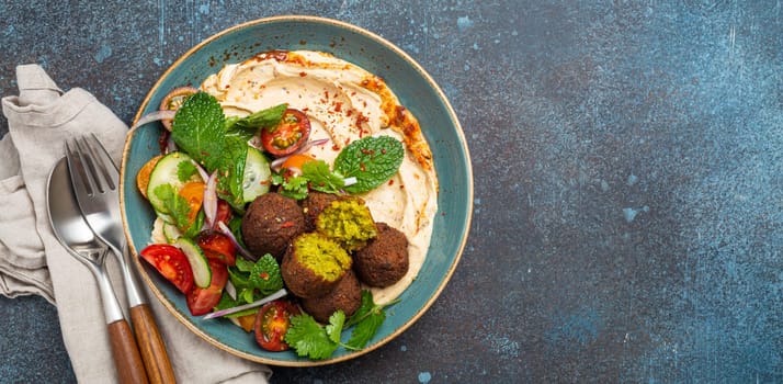 Middle Eastern Arab meal with fried falafel, hummus, vegetables salad with fresh green cilantro and mint leaves in ceramic bowl on stone rustic background top view. Arabic cuisine, space for text